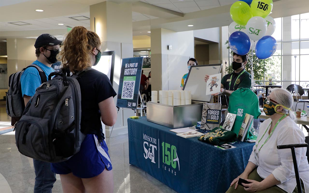 Students stand around table with promotional items and time capsule.